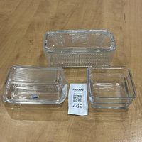 Set of three clear glass refrigerator dishes with two lids on wooden surface