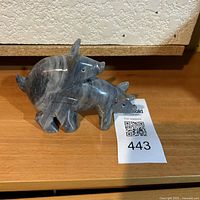 Polished stone pig figurine sculpture with label on shelf front, showing front and side pig positions
