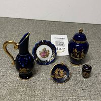 Full view of 5 piece miniature porcelain set with cobalt blue and gold decoration showing handled jug, two jars, and two small plates.