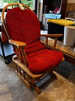 Front view of the wooden glider rocking chair with red cushions. Shows full chair and cushion detail.