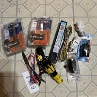 Overview of lot showing two packaged Rona door handles, Philips Advance lighting ballast with wiring, voltage tester, multiple light socket adapters, and plug in mixed condition.