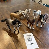 All six Schleich horse figurines arranged on wooden table alongside a MaxSold auction tag showing lot 338. Horses vary in color and size including foal and adults.