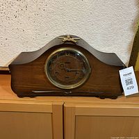 Front view of the Seth Thomas wooden mantel clock with curved silhouette and brass bezel glass door.