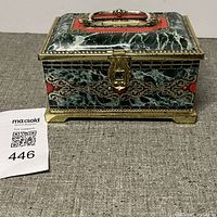 Front view of vintage tin box showing ornate faux marble design, gold-tone accents, clasp, and handle on lid.