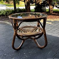 Full view of the vintage rattan bamboo side table showing the round glass top, curved rattan frame and woven circular lower shelf.