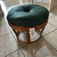 Vintage round rattan ottoman with removable dark green cushion on top, showing overall condition and cushion detail.