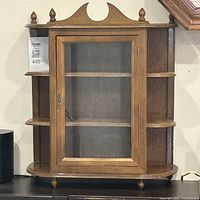 Front view of wood and glass curio cabinet showing the glass door, lock, and side shelves.