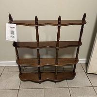 Front view of the wooden wall-mounted shelf showing four shelves with wavy edges and turned spindle supports, medium brown color.