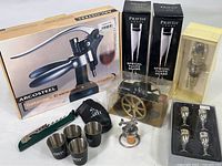 Overall lot showing boxed Arcosteel corkscrew, boxed Pravda glasses, Cutty branded metal shot cups with pouch, vintage airplane motif bottle stopper, Mango Moon bottle stopper, miniature aperitif cups and Courvoisier cannon replica, Wente Vineyards corkscrew with green handle.