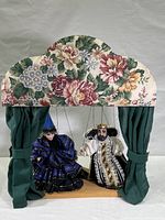 Full view of marionette stage and two puppets with floral canopy and green curtains.