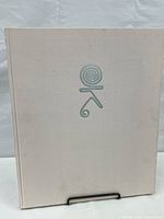 Front cover of the hardcover art book with beige cloth cover and silver spiral design.