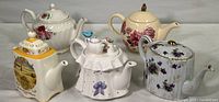 Five unique decorative teapots arranged on a white surface, showing their shapes and patterns.
