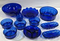 Overview of the entire collection showing two large bowls, four small bowls, grape motif plate, divided plate, bud vase, and two oblong serving dishes, all in cobalt blue glass.