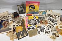 Photo showing an assortment of black and white photos, photo slides, vintage sheet music, an MGM Singing in the Rain record, used Disneyland coupon book, old dictionary, and other printed material spread on a table.