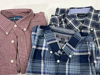 Photo showing all three shirts folded: red and white Ralph Lauren, blue Tommy Hilfiger, and navy Nautica, all with button-down collars.