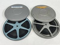Two metal 8mm film reels with matching metal cans. One can labeled 'Woody Woodpecker', the other 'Laurel & Hardy'. Films appear intact in reels.