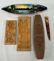 Full view of the grouped items showing hand painted canoe, cookie molds, candy mold, and letter opener on white fabric background.