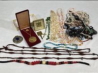Full display of lot contents arranged on table showing medallion, clock, brooch, and assorted necklaces of different materials.