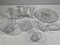 Full view of all glassware items including candlesticks, bud vases, footed dishes, and serving plates arranged on surface