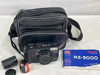 Camera with case, two film rolls, and user manual arranged for overview.