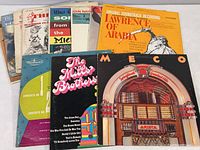 Overview of 11 vintage vinyl record albums showing a mixture of soundtracks and various music genres. Covers include Lawrence of Arabia, The Mills Brothers, and Meco albums.