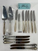 Top view of cutlery pieces including 7 Wallace Firenze butter spreaders, 2 serving knives, 5 Reed & Barton sterling handle table knives, and original Firenze sterling tag box.