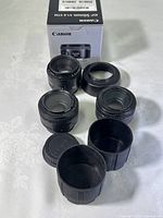 Three Canon EF mount 50mm f/1.8 lenses arranged with lens caps, hoods and original box visible.