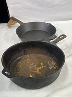 Two cast iron skillets placed on a white surface, one new and clean, one heavily used with rust.
