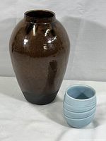 Photo showing both the brown ceramic vase and the smaller light blue ceramic cup side by side, highlighting size difference and design.