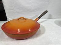 Side angle showing the full orange to red gradient enameled lid and the skillet with wooden handle.