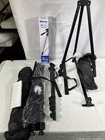 Photo showing the DYNEX monopod, Ultimaxx tripod, multiple telescoping pop-up display screens, black carrying bags, and instruction manual all laid out flat on a surface.