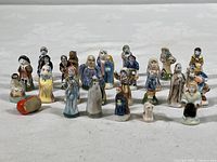 Overview photo showing 28 multicolored French Feve bean porcelain nativity miniature figurines arranged on a white surface.