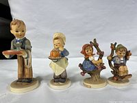 Four Goebel ceramic figurines from West Germany on white cloth background, showing full set of 4 including the boy with tray, girl with cake, and two children with tree branches