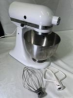 Full view of KitchenAid Classic stand mixer in white with stainless steel bowl and included whisk and paddle attachments on the side.