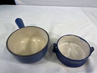 Two blue hand-painted ceramic cookware pieces on white surface: a larger handled pot and a smaller two-handled pot