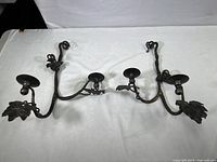 Two vintage wrought iron wall-mounted candle holders with grapevine motifs laid on a white surface.