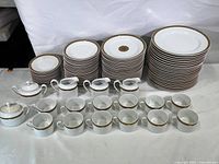 Full set of Rosenthal Renaissance Catarina porcelain dinnerware displayed, showing stack of plates in various sizes with gold decorative banding, coffee cups, and serving pieces in front.
