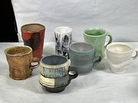 Seven multi-colored ceramic mugs arranged in a group showing various colors, shapes, and sizes