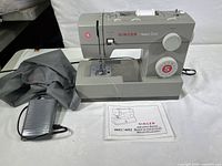 Full view of the Singer sewing machine with foot pedal, thread spool, and instruction manual.