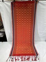 Full view of the textile showing red and gold pattern with multicolor striped borders and tassels at the edge.