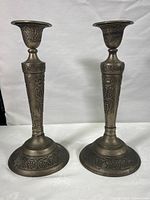 Pair of vintage ornate brass candlesticks with grapevine and floral designs, standing on white fabric background.