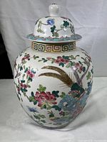 Front view of vintage Chinese porcelain ginger jar vase decorated with famille rose floral and bird patterns, showing lid and main body with gold and multicolor details.