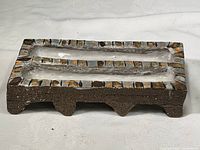 Front angled view of the rectangular handmade stoneware incense dish showing mosaic tiled edge accents and grooved channels to hold incense sticks.