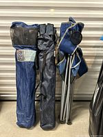 Three blue camping chairs folded and packed in their matching blue carrying bags with shoulder straps