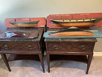 Four nautical wooden plaques featuring hand-carved ships and whale figure displayed on dark wood side tables.