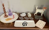 Wide view of 13-piece eclectic decor set on wooden surface showing tray, candle holders, dog figurine, ashtrays, soap, decorative dish and beaded ornament.