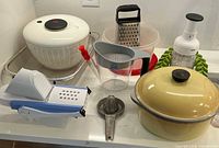 Photo showing various pieces of kitchenware including salad spinner, mandolin, grater, juicer, chop, stew pot, and more