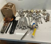 Wide view of all assorted silverware, utensils, and wooden caddy displayed on countertop.