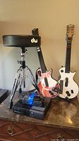 Photo showing DW branded adjustable height chrome drum stool, two Guitar Hero guitar controllers, Xbox 360 console below