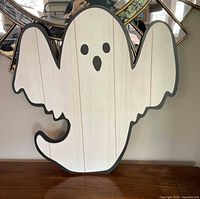 Front view of wooden ghost Halloween decor showing painted face with black eyes and mouth, white painted body with wood grain lines visible.
